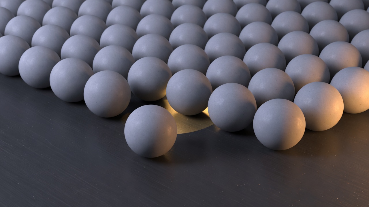 Gray spheres packed on a dark table, with one sphere pulled forward out of the pack