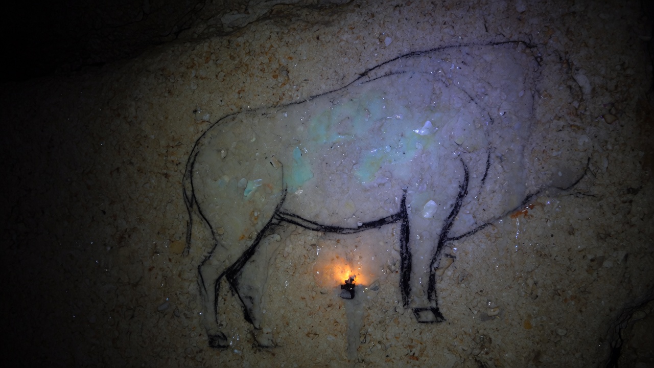 A dark cave wall with a black charcoal line under a pale blue-green film and a small orange glow